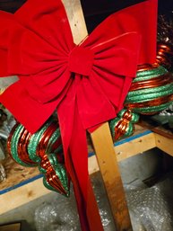 Large Red Velvet Holiday Bow Paired With 2 Glittery Green And Red Swirled Finial Ornaments.