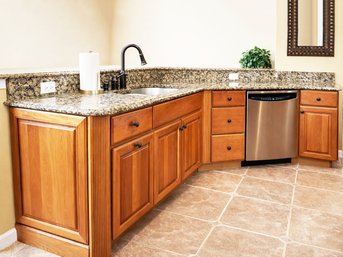 A Custom Cherry Base Cabinet Run With Granite Counter And Bar Including Undermount Sink And Bronze Faucet