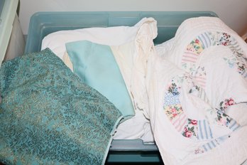 A Quilt & Different Colored Fabrics In Plastic Bin