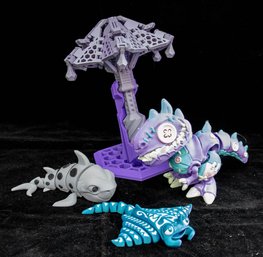 Articulated, 3D Printed Toys Purple Dinosaur Figure, A Stingray Figure, A Shark Figure, And A Display Stand