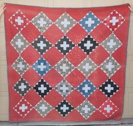 Vintage Quilt Featuring A 'Monkey Wrench' Or 'Churn Dash' Design Made From Various Patterned Fabrics On A Red