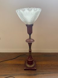 A Decorative Table Lamp With A Ribbed Glass Shade And Red Metal Base