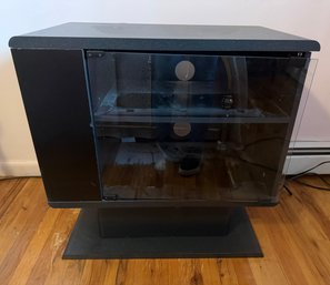 Black Media Stand Featuring Glass Door And An Inner Shelf