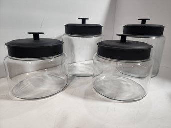 #87 LOT OF 4 MATCHING GLASS CANISTERS WITH BLACK METAL LIDS