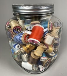 Glass Canister Full Of Spools Of Thread
