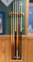 Collection Of Six Pool Cues With A Wall Mounted Storage Rack