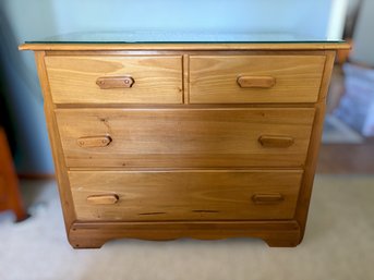 Warm Pine Chest Of Drawers Featuring Glass Top, Wood Pulls, And Four Drawer Storage