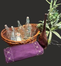 Lot Consists Of A Decorative Handled Basket, Various Clear Bottles, Tall Vase, Silk Plant And 2 Placemats