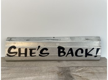 Galvanized Metal Sign With Black Painted Text Reading SHE'S BACK!