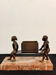 Two Small Bronze Figurines Carrying A Basket On Marble Plinth