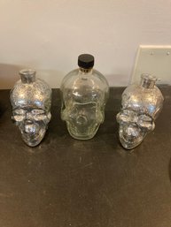 Two Skull Candle Holders And A Glass Bottle