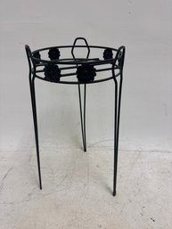 Black Metal Plant Stand With A Flower Medallion Rim Design And Hairpin Legs.